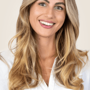 Woman with long wavy hair smiling against a beige background representing color service. Link goes to Services page.