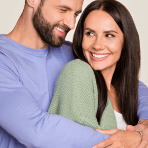 A smiling couple embracing, the man in a lavender shirt and the woman in a green cardigan representing the waxing services. Link goes to services page.