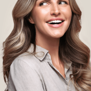 Woman smiling with long, wavy hair and a light-colored shirt representing blowouts service. Link goes to services page.